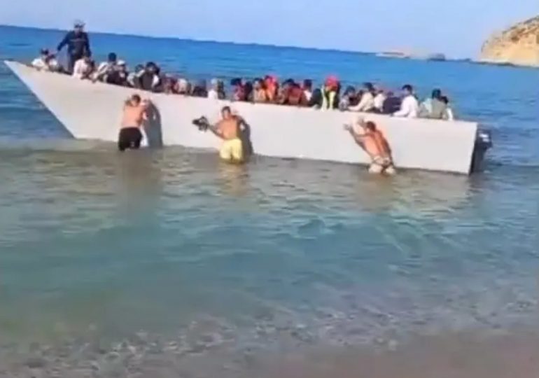 Staggering moment beachgoers push packed migrant boat BACK off Greek tourist beach after they sailed across from Libya